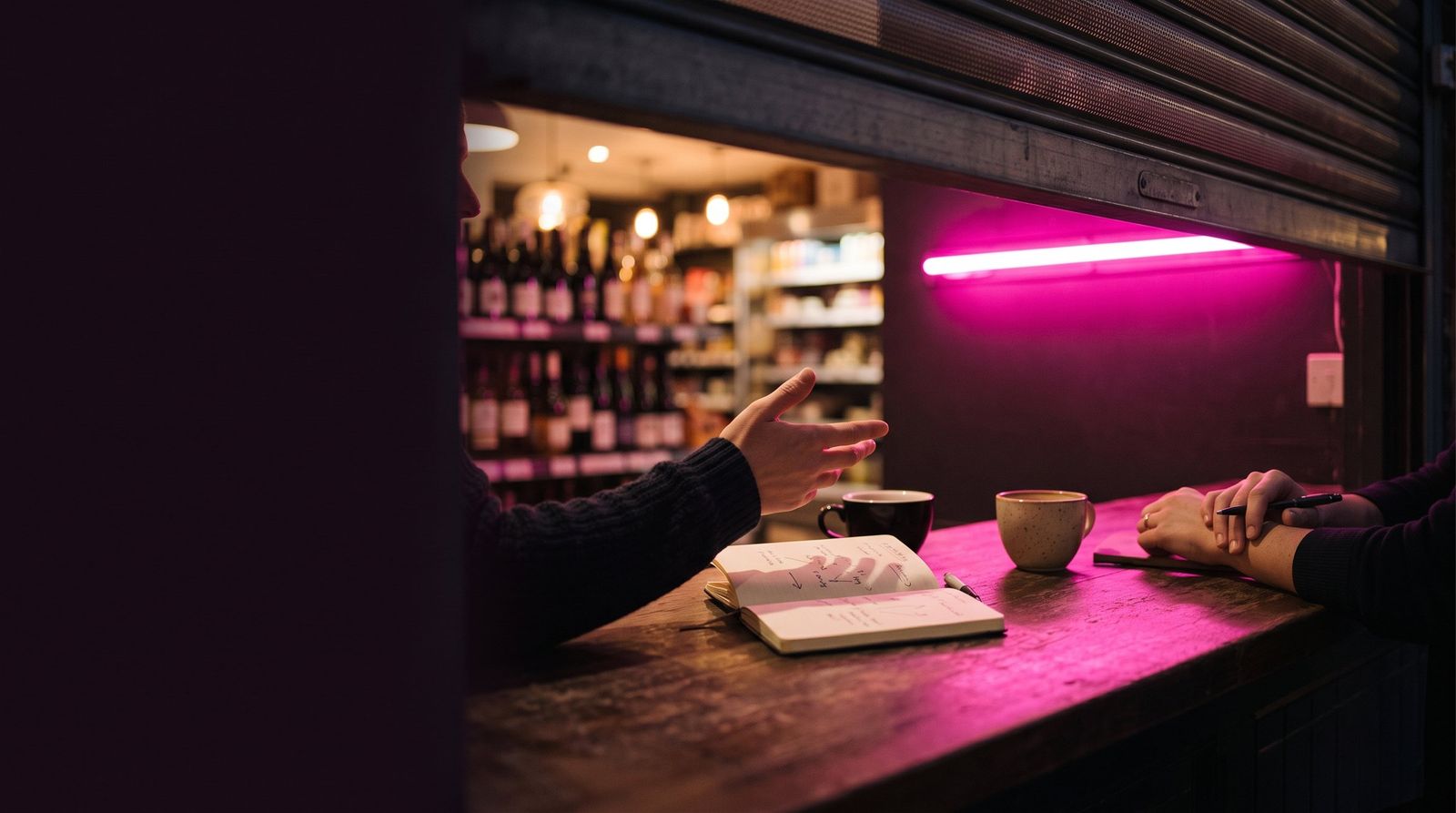 Mostrador de una tienda al cerrar, con la persiana a medias y un neón fucsia